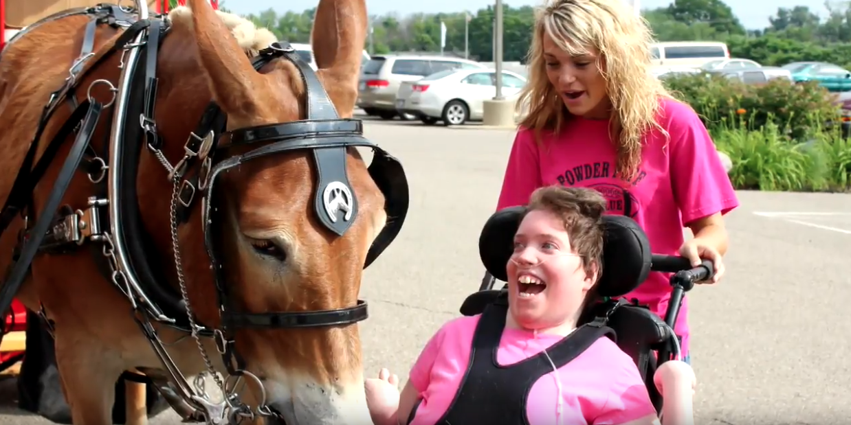 A woman in a wheel chair smiles near a horse. Another woman stands behind her.