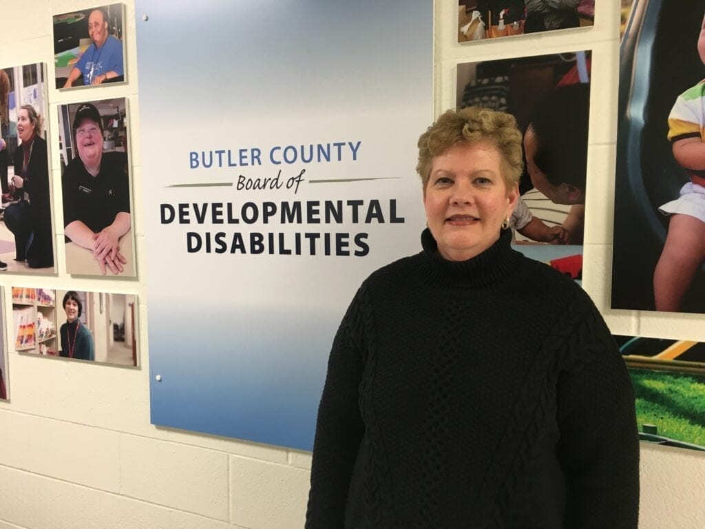 Una mujer delante del logotipo de Butler County Board of Developmental Disabilities. Sonríe directamente a la cámara.