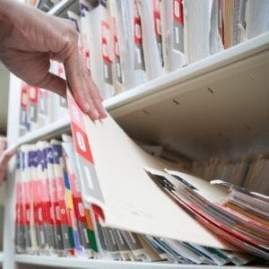 A hand pulls a file from a shelf full of files.