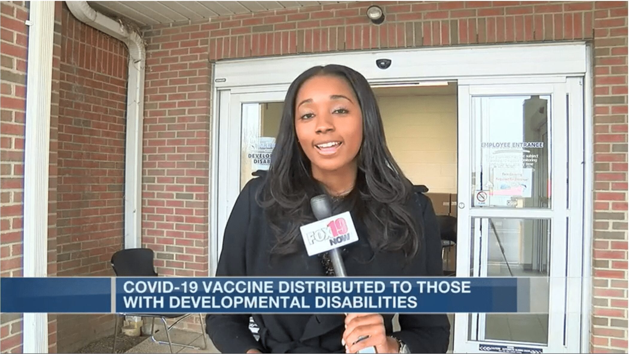 A woman with a FOX19 microphone stands in front of a building. A caption reads: COVID-19 vaccine distributed to those with developmental disabilities.