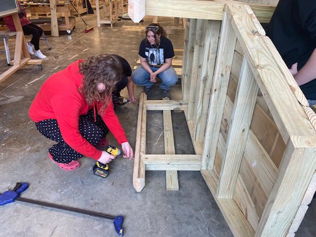 Two women using a drill to assemble a playset