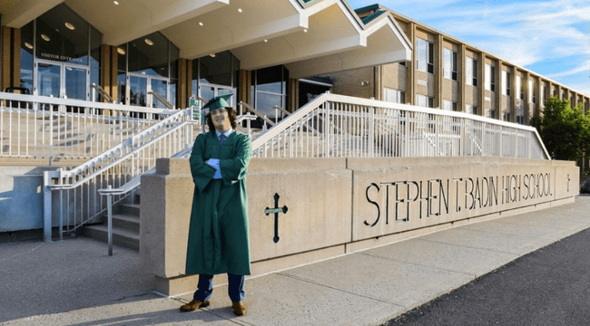 A man with a green graduation cap and gown on outside in front "Stephen Badin Highschool"