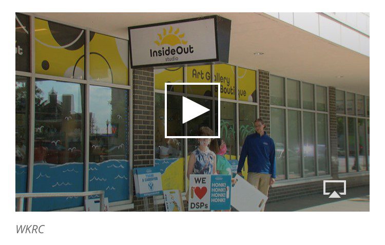 3 people standing outside in front of a building holding signs