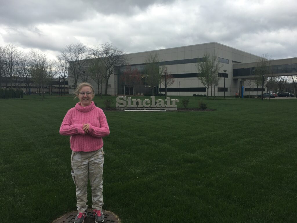 Una mujer al aire libre en la hierba con el Sinclair Community College al fondo.