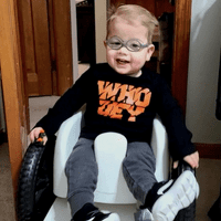 Boy in a wheelchair indoors with glasses and a bengals shirt on