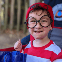 a boy outdoors with glasses and a red hat on smiling for a photo