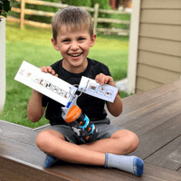 a boy outdoors sitting on a deck with two papers in his hands