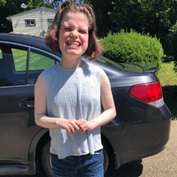 A woman standing outdoors in a driveway in front of a car