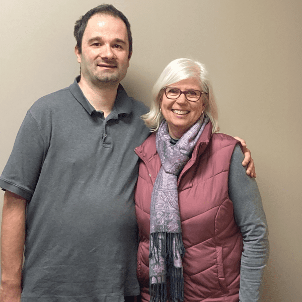 A man and a woman standing indoors against a beige wall side by side smiling