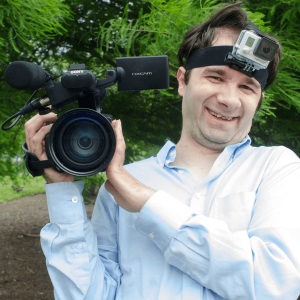 A man outdoors by trees holding a camera