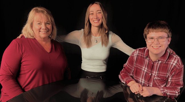 3 women indoors sitting together at black table smiling