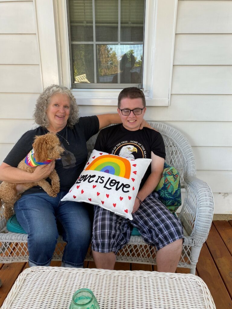 a women and a man outdoors sitting on a porch on a couch holding a dog and pillow