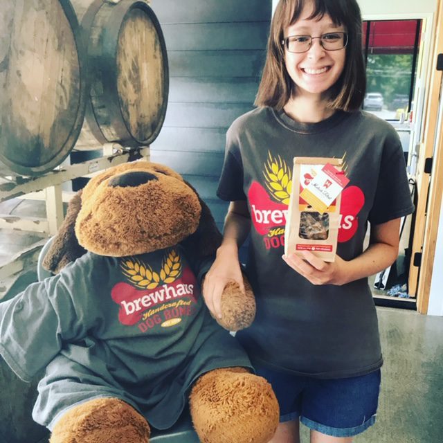 A woman indoors holding a bag of dog bones standing next to a stuffed animal dog