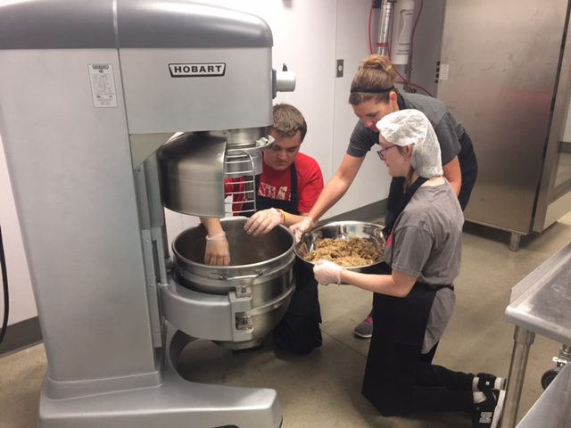 3 people in a kitchen using a baking mixer 