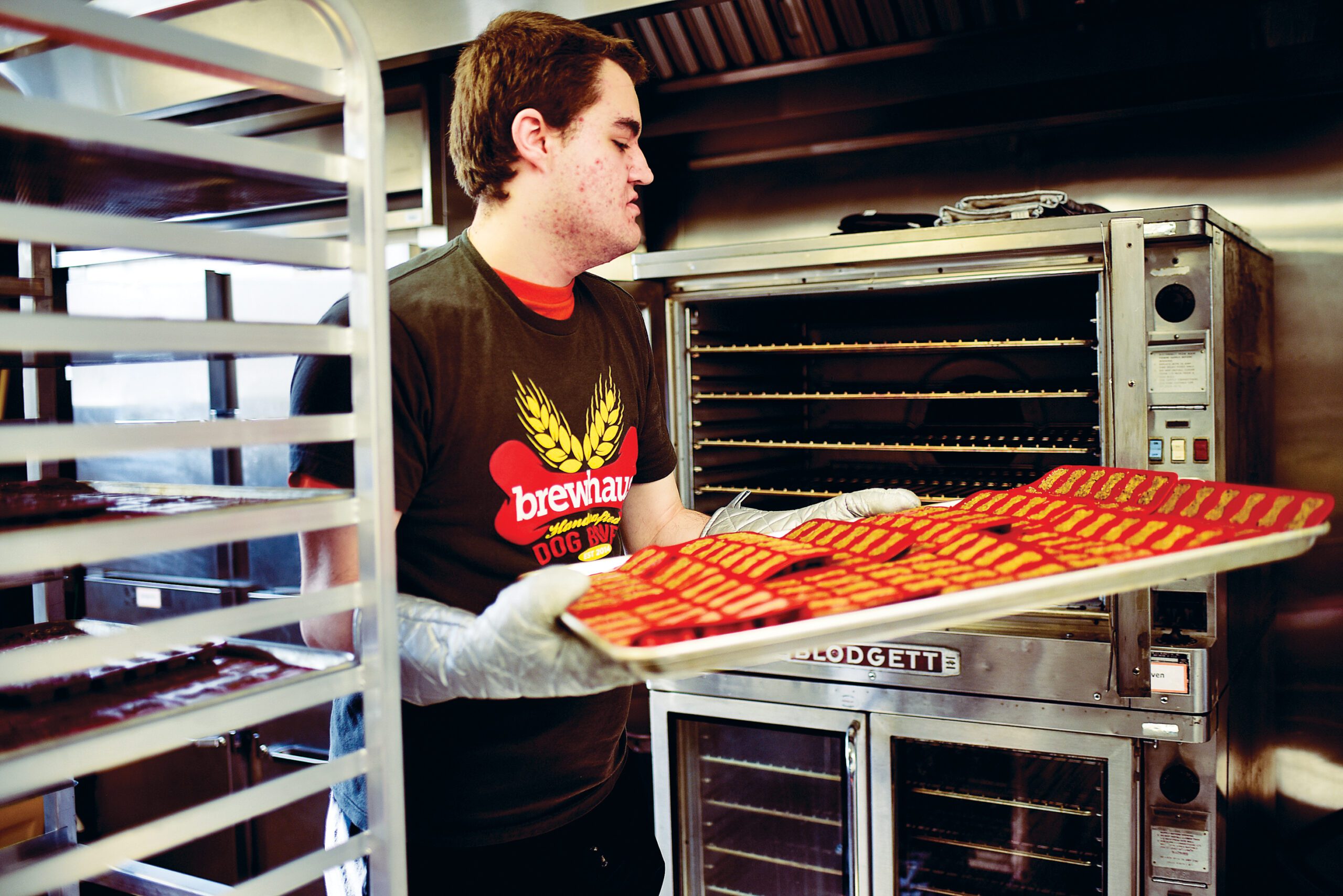 a man in a kitchen taking a tray of dog bones out of the oven