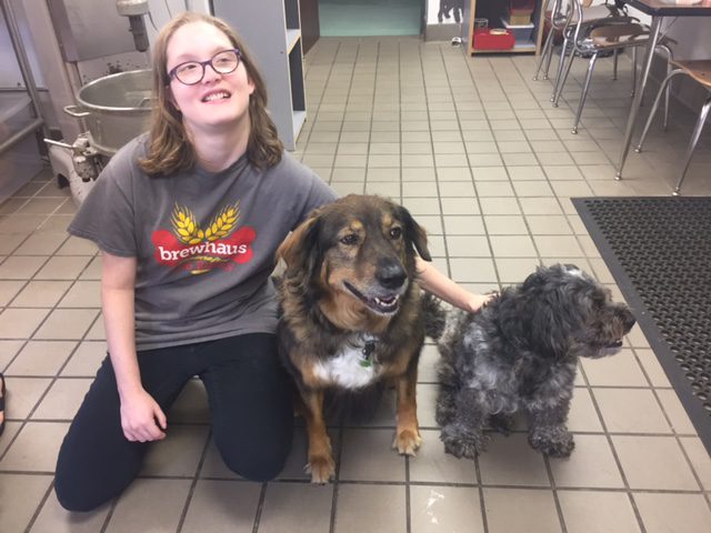 a women kneeling next to 2 dogs in a kitchen