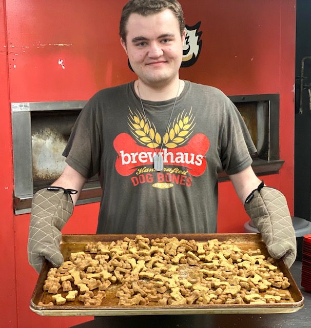 a man in a kitchen holding a tray of baked dog bones