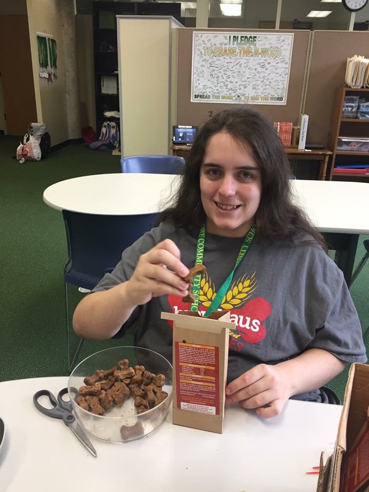 a woman indoors sitting at a table weighing out dog bones and placing them into a bag