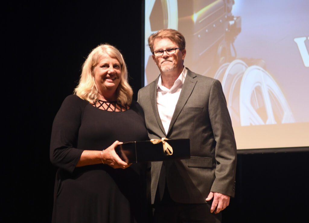 A man and a woman indoors on stage holding an award