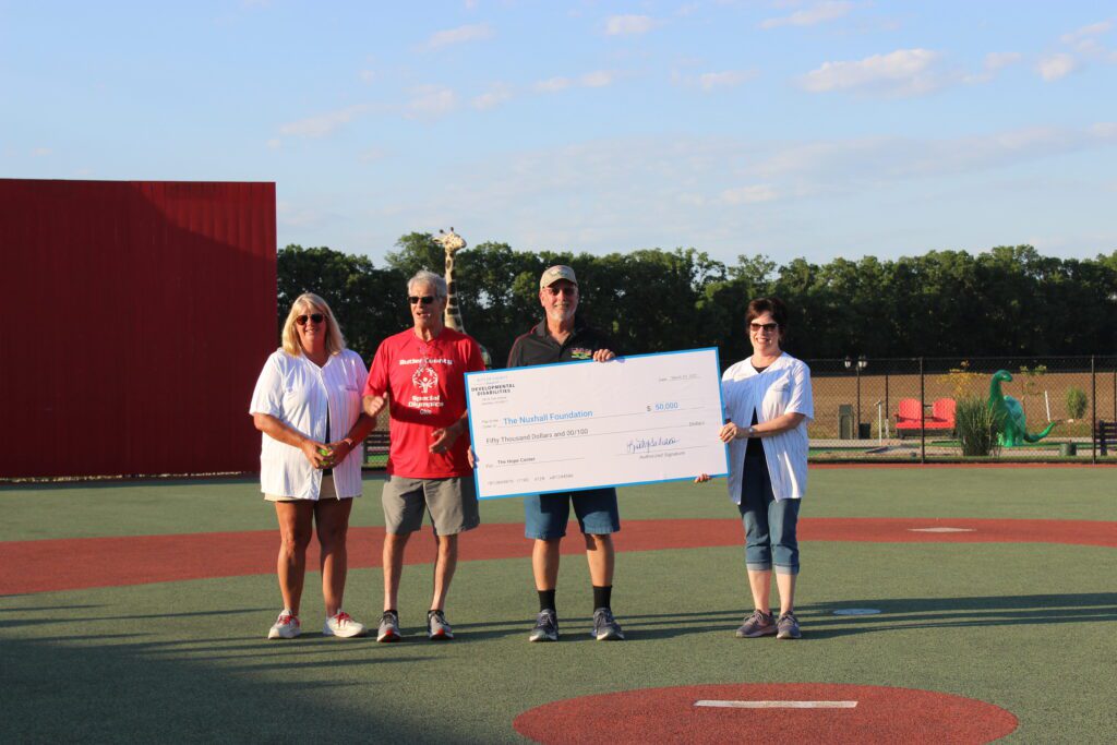4 people on a baseball field holding a large cardboard check