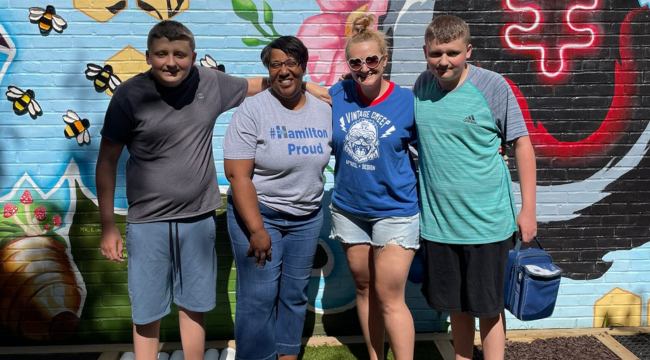 4 people standing outside in front of a wall of art smiling for a photo