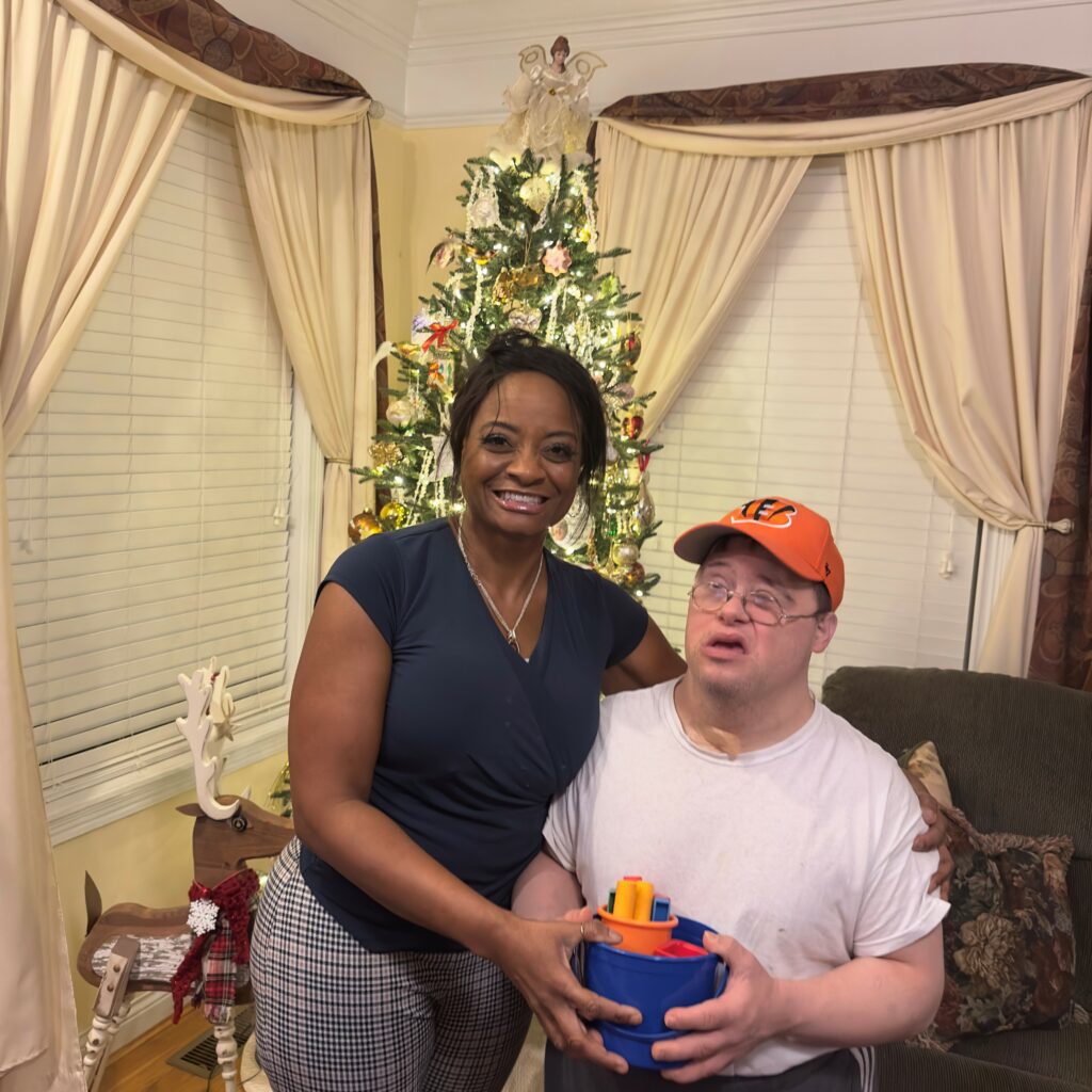 A man and a women indoors sitting in a chair in front of a Christmas tree.