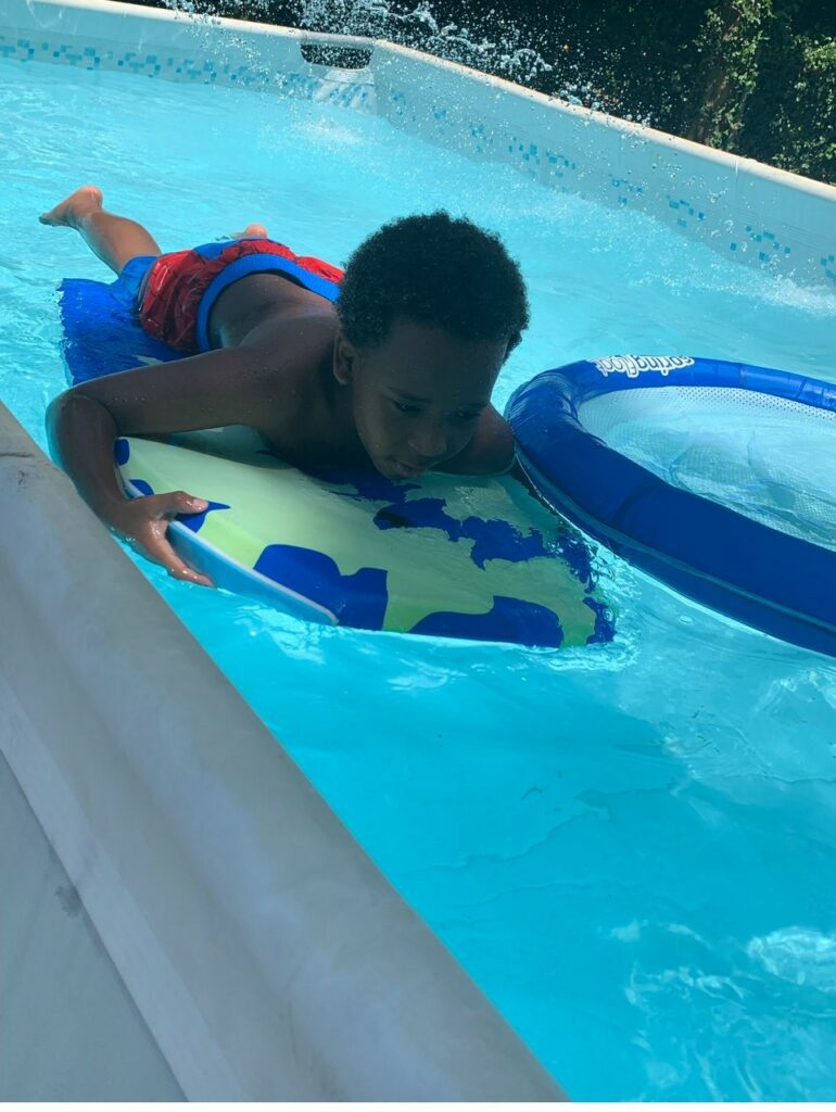 A child outdoors on a pool floaty swimming in a pool.