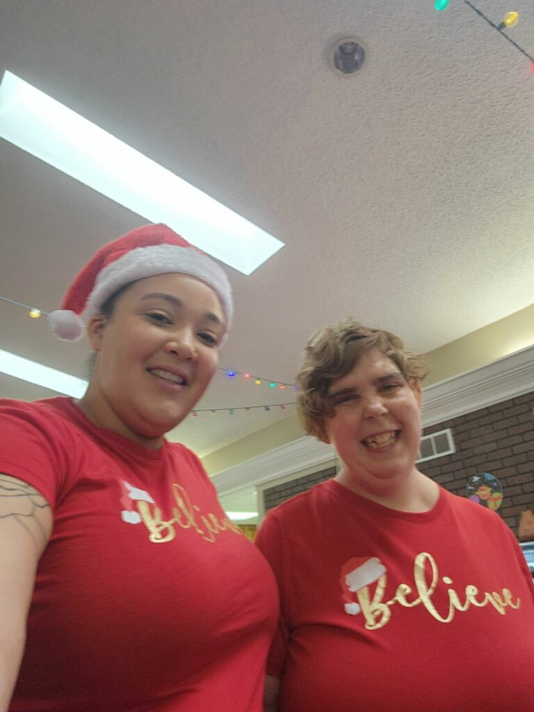 2 women side by side smiling indoors with red t shirts on