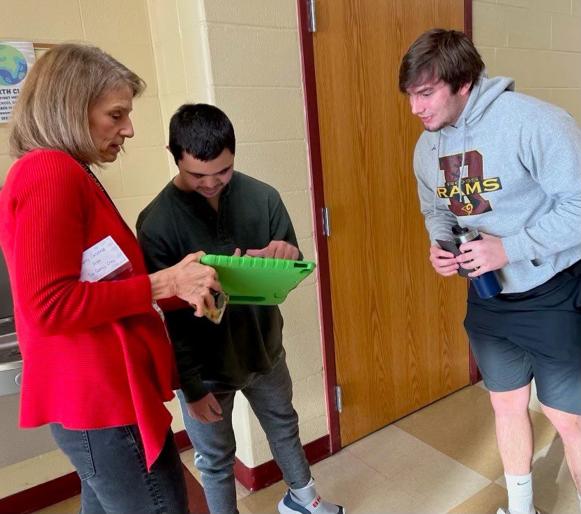 a teacher and two students indoors looking at an iPad