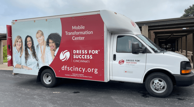 a truck with a picture of a woman with text that says, Mobile Transformation Center, Dress for Success Cincinnati, dfscincy.org, outdoors in front of a building.