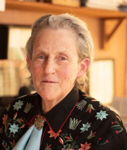 An older, distinguished looking woman wears a western shirt with embroidered flowers and a bolo tie with the initials TG engraved as an emblem. 