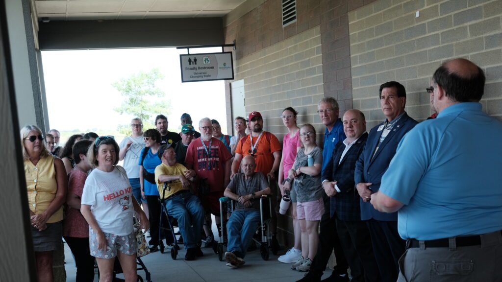 A crowd of people gather in a large brick hallway. A sign hangs on the wall above the group. It reads Family restroom Universal Changing Table.