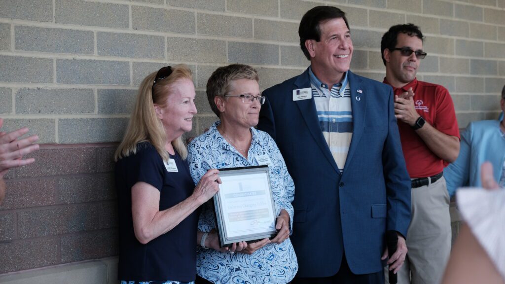 Four people stand together. Two of them hold a plaque. Light on the plaque makes the text indistinguishable.